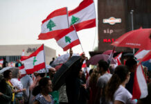 Crowd holding Lebanese flags and umbrellas in city.