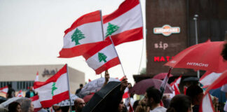 Crowd holding Lebanese flags and umbrellas in city.