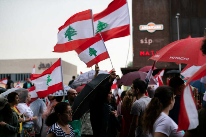 Crowd holding Lebanese flags and umbrellas in city.