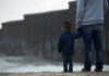 Adult and child standing near border wall beach