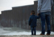 Adult and child standing near border wall beach