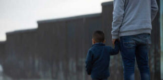 Adult and child standing near border wall beach