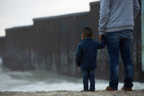 immigrant-kids1955431621 Adult and child standing near border wall beach