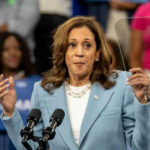 Kamala Harris’s Campaign CHAOS: The Untold Story Woman in light blue blazer speaking at podium with microphones
