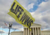 Yellow Life Wins flag near government building cloudy sky
