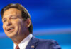 Man in a suit speaking against a blue backdrop