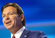 Man in a suit speaking against a blue backdrop