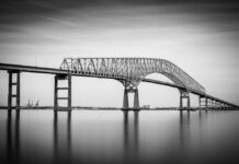 Baltimore’s Bridge Collapse: Hidden Truths Emerge A large bridge spanning over a calm body of water in black and white