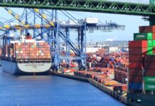 Pandemic Cartel UNMASKED – DOJ Exposes Chinese Scheme A cargo ship loaded with colorful containers docked at a busy shipping port