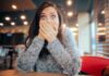 A surprised woman covering her mouth with her hands in a casual indoor setting