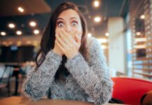 A surprised woman covering her mouth with her hands in a casual indoor setting