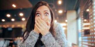 A surprised woman covering her mouth with her hands in a casual indoor setting