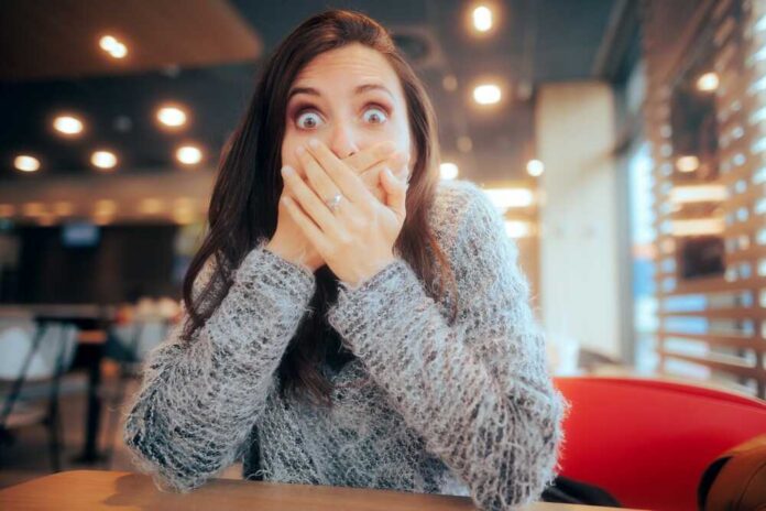 A surprised woman covering her mouth with her hands in a casual indoor setting