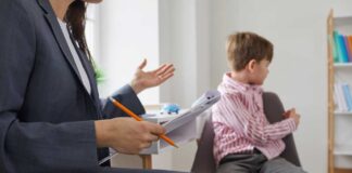 A child sitting on a chair while a professional gestures with a notepad and pencil