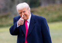 Trump’s Jaw-Dropping Visit to China’s Power Hub A man in a dark coat and pink tie giving a thumbs up outdoors