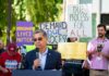 Speaker addressing a crowd at an immigration rights rally with protest signs in the background