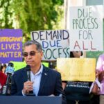 Becerra’s Shadow Army: Who’s Really Canvassing? Speaker addressing a crowd at an immigration rights rally with protest signs in the background