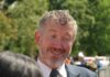 A smiling man in a suit engaging in conversation outdoors
