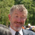 A smiling man in a suit engaging in conversation outdoors