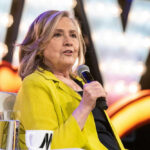 Person in yellow jacket speaks into microphone.