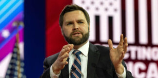 Man in suit speaking on stage with gesturing hands