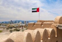 Arsonist–Firefighter: Abu Dhabi’s Iran Play UAE flag waving atop a historic fort with a city skyline in the background