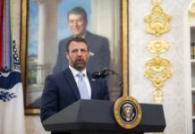 Man in suit speaking at a podium in an ornate room