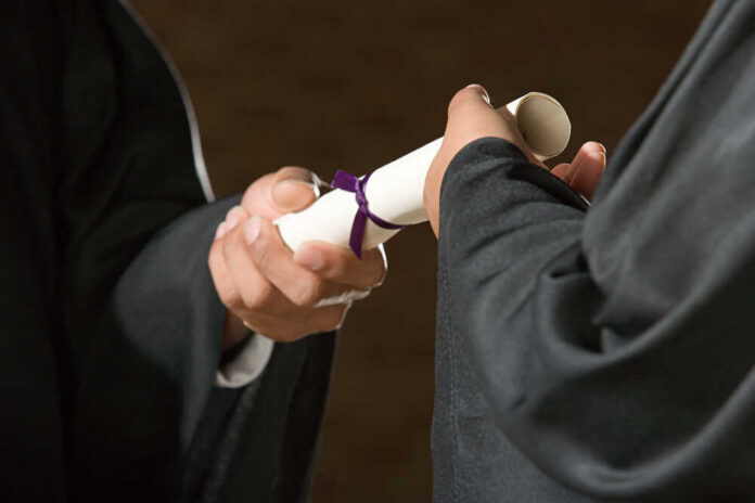 Two individuals exchanging a diploma during a graduation ceremony