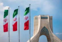$300B Carrot—Does Tehran Keep The Bomb? Three Iranian flags in front of the Azadi Tower against a blue sky