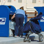 Postal worker loading mail into a blue USPS collection box