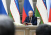UN Files Shred Putin’s Civilian Story man in suit speaking at a conference table with microphones and flags behind