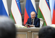 UN Files Shred Putin’s Civilian Story man in suit speaking at a conference table with microphones and flags behind