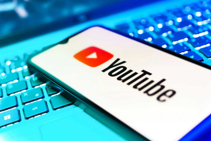 YouTube app on smartphone over illuminated laptop keyboard