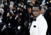 Man in white tuxedo surrounded by photographers.