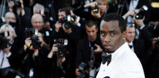 Man in white tuxedo surrounded by photographers.