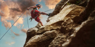 Person rock climbing with ropes against a cloudy sky