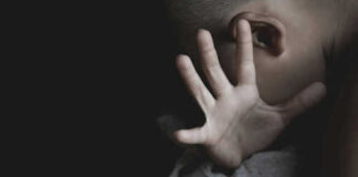 Child covering face with hand in dim light