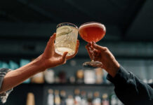 Fugitive CEO Parties In Munich — Girlfriend In The Crosshairs Two hands clinking cocktails