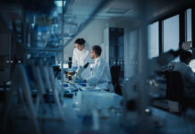 Mystery Parasite Rips Through 31 States Two scientists working in a laboratory with a microscope and computer screens