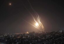 Night sky above a city with multiple rockets arcing and bright explosions