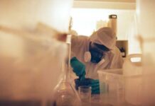 Novichok Denials Collide With British Intel Scientist in protective gear mixing substance in a lab