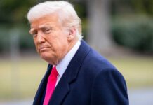 Library Dedication Sparks MAGA Frenzy A political figure with a serious expression, wearing a dark coat and a bright tie, outdoors