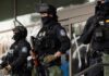 Riot police in tactical gear stand guard outside a building