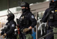 Pardoned—Then Vanished: ICE Moves Fast Riot police in tactical gear stand guard outside a building