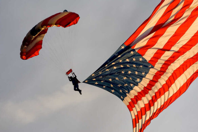 A,Sky,Diver,Carries,An,American,Flag,As,He,Descends Skydiver descending with a large American flag parachute