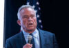 Dana Bash Stunned As RFK Jr. Hits Back Man holding microphone, speaking with American flag behind.