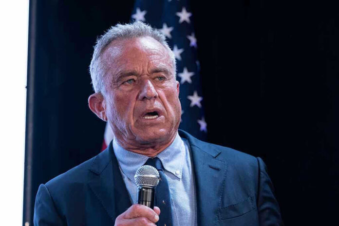 2456684675 Man holding microphone, speaking with American flag behind.