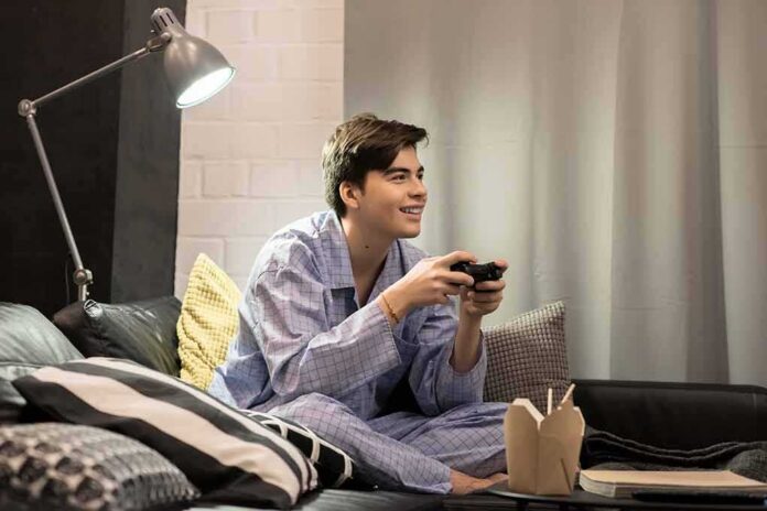 Teen in pajamas playing video games on a couch
