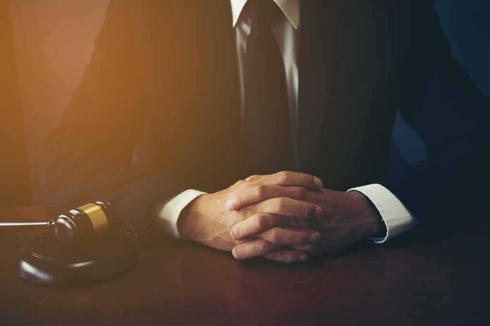 shutterstock_1049502869 person in suit with hands clasped at a desk beside a gavel