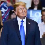 GOP Room ERUPTS — Trump Name Triggers Fury man in navy suit with blue tie at crowded indoor event